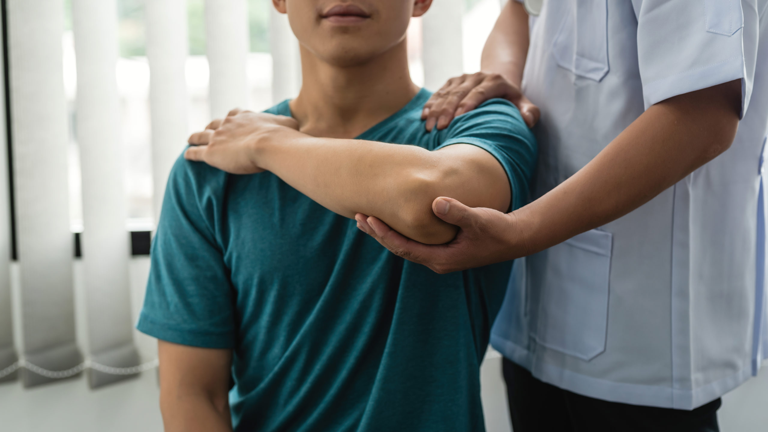 Man physiotherapist assisting male patient with elbow injury at